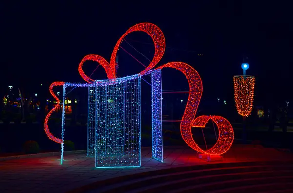 Aydınlatılmış bir hediye kutusu, fiyonklu ve şelaleli ışıklar, şenlikli bir sokak Noel süsü gibi mükemmel uyuyor, gece ayarı için neşeli bir parıltı ekliyor.