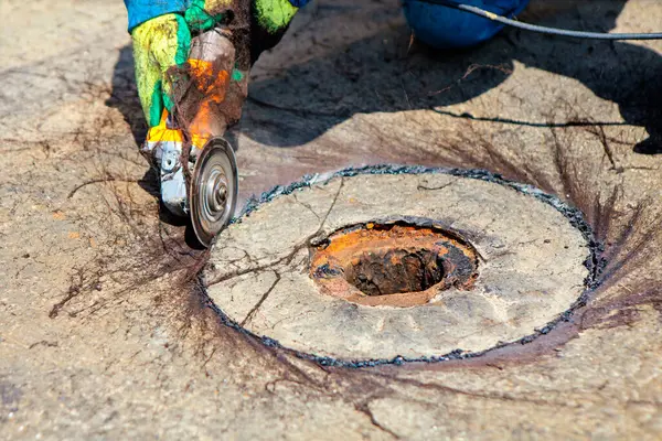 İşçi tam olarak çatının bir bölümünü kesmek için döner kesici kullanır. Kanalizasyon deliğinin etrafındaki çatının hassas kesimi. Çatıdaki beton rögar kapağını kesmek için el yapımı dairesel testere.