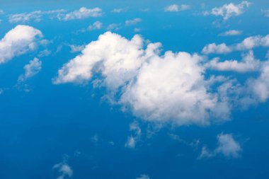 Bulutlar denizin üzerindeki masmavi gökyüzünde sürükleniyor. Bulutların nefes kesen manzarası, parlak mavi bir arka plana karşı. Kümülüs bulutları, pamuk şeker gibi, uçsuz bucaksız mavi bir cennette huzur içinde süzülür.