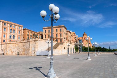 Cagliari 'deki Bastione San Remy Meydanı' nda zarif sokak lambaları olan geniş asfalt bir plaza bulunuyor. Arka planda, önemli merdivenleri olan tarihi binalar kubbeli bir binaya çıkıyor.
