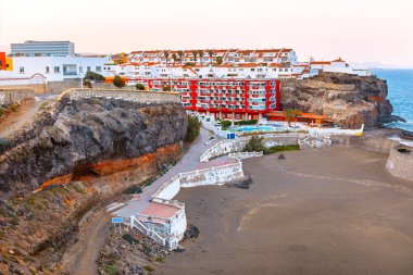 Playa San Borondon, Gran Canaria 'nın kayalık manzarası, teraslı binalar, kumlu sahil ve yumuşak akşam ışığı altında Atlantik Okyanusu. Seyahat ve mimari temalar için ideal sakin kıyı sahnesi