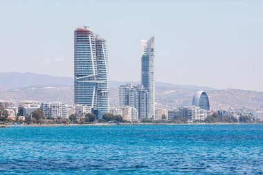 Kıbrıs 'ın Limasol kentinin modern silueti, Akdeniz kıyısı boyunca ikonik yüksek binalara sahip. Berrak mavi sular ve güneşli bir gökyüzü şehrin lüks ve sahil cazibesinin dinamik karışımını vurgular