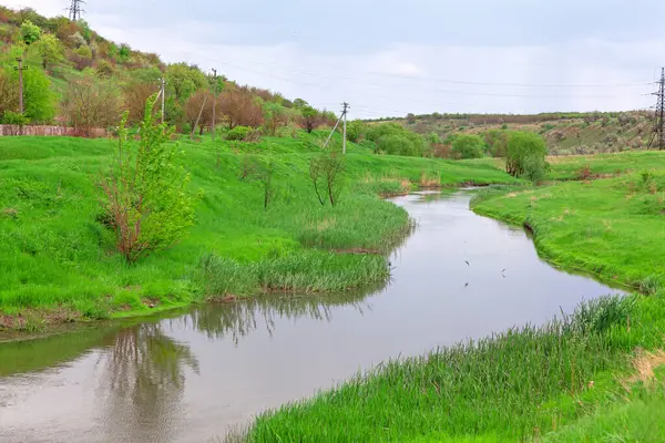 Moldova 'daki Serene River Raut bulutlu gökyüzünün altındaki ağaçlar ve çalılarla kaplı yemyeşil yamaçların arasından süzülüyor. Elektrik hatları doğal güzelliğe ince insan unsurları ekleyerek araziye yayılıyor.