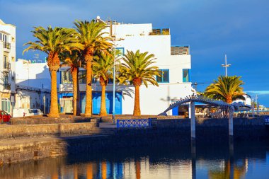 Arrecife 'deki sakin limanda, durgun suya yansıyan beyaz binalar ve yüksek palmiye ağaçları bulunuyor. Benzersiz kıvrımlı köprü ve altın güneş ışığı bu Lanzarote kasabasının güzel sahil cazibesine katkı sağlıyor.