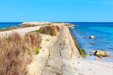 Kıyı yolu taştan bir deniz yatağı boyunca kıvrılarak durgun turkuaz sulara çıkar. Yol, sakin bir sahile ve derin mavi denize uzanan taştan bir deniz kenarına uzanıyor.