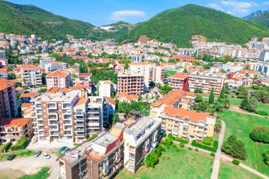 Karadağ 'ın Budva kentinin hava manzarasında yeşil tepeler ve dağlar arasında inşa edilmiş renkli binalar yer alıyor. Modern ve geleneksel mimari ve yemyeşil manzaralar 