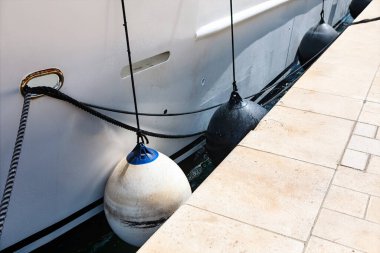 Beyaz yat rıhtımda güvenli bir şekilde dinleniyor, halatlar ve çamurluklarla bağlanmış. Siyah ve beyaz çamurluklar, halatlarla asılmış, tekneyi limanda sabit tutun.