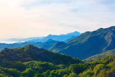 Katmanlı dağların engin manzarası, yumuşak mavi bir sise dönüşüyor. Dağların engebeli güzelliği, sabahın yumuşak ışıklarına doğru yayılıyor. Dağ manzarasının sakin manzarası