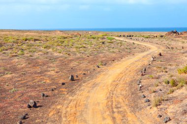 Uzak bir okyanusa doğru uzanan toprak yol kurak arazide esiyor. Issız ama güzel bir volkanik ovanın içinden geçen ıssız bir patika.