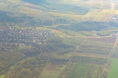Kırsal alan, tarlaların ve yerleşim alanlarının karmaşık yerleşim yerlerini gösteriyor. Ekinler yayılıyor, bir ev kümesi ile noktalanıyor, kırsal yaşamın görsel bir temsili.