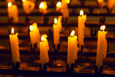 Sıcak mum ışığı, sıra sıra dizilmiş birden fazla mum üzerinde hafifçe titreyerek sakin ve düşünceli bir atmosfer yaratır. Parlak mum alevleri huzur, yansıma ve sükuneti çağrıştırır.