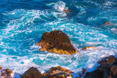 Canlı turkuaz dalgalar engebeli kıyı kayalarına çarparak hareket ve enerji dolu dramatik deniz manzarası yaratır. Güç, seyahat, macera ve doğa güzelliği temaları için mükemmel doğal bir sahne.
