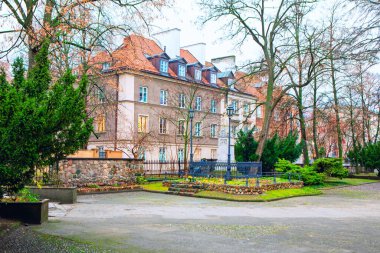 Polonya 'nın Varşova kentindeki bir şehir parkında kırmızı kiremit çatılı ve çıplak ağaçlara sahip tarihi Avrupa mimarisi. Büyüleyici şehir manzarasında sonbahar atmosferi