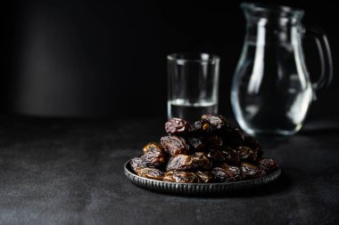 Dates fruit on oriental plate on dark background. Dried organic Superfood. Water for Ramadan fasting. Traditional muslim iftar food