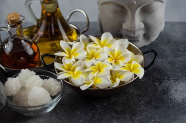 Spa massage relax composition setting. Natural essence oils, sea salt, towel, candles, Buddha head statue and plumeria frangipani exotic flowers. Gray colors.