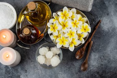 Spa massage relax composition setting. Natural essence oils, sea salt, towel, candles and plumeria frangipani exotic flowers. Gray colors.