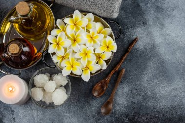 Spa massage relax composition setting. Natural essence oils, sea salt, towel, candles and plumeria frangipani exotic flowers. Gray colors.