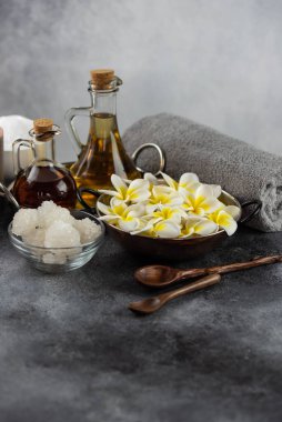 Spa massage relax composition setting. Natural essence oils, sea salt, towel, candles and plumeria frangipani exotic flowers. Gray colors.