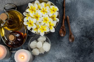 Spa massage relax composition setting. Natural essence oils, sea salt, towel, candles and plumeria frangipani exotic flowers. Gray colors.