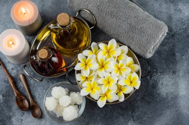 Spa massage relax composition setting. Natural essence oils, sea salt, towel, candles and plumeria frangipani exotic flowers. Gray colors.