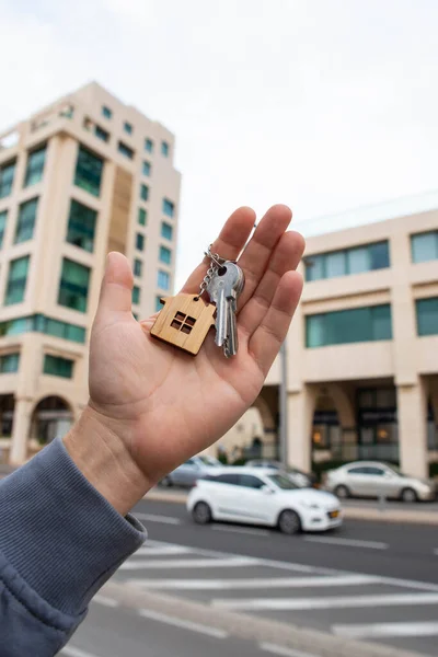 Buying a house, building repair and mortgage concept. Estimation real estate property with loan money and banking. Keys with toy home keychain charm in hand on city building background.