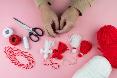 Woman making handmade traditional martisor, from red and white strings with tassel. Symbol of holiday 1 March, Martenitsa, Baba Marta, beginning of spring in Romania, Bulgaria, Moldova