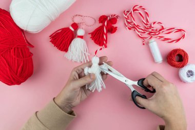 Woman making handmade traditional martisor, from red and white strings with tassel. Symbol of holiday 1 March, Martenitsa, Baba Marta, beginning of spring in Romania, Bulgaria, Moldova