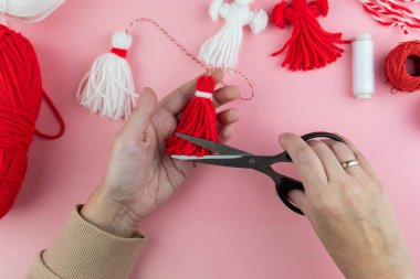 Woman making handmade traditional martisor, from red and white strings with tassel. Symbol of holiday 1 March, Martenitsa, Baba Marta, beginning of spring in Romania, Bulgaria, Moldova