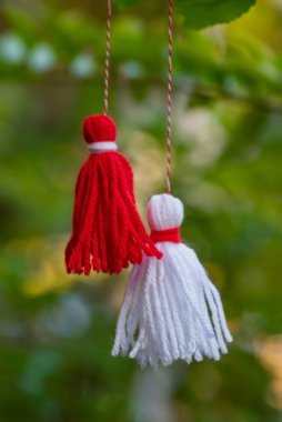 Traditional Martisor on green tree branch - symbol of 1 March, Martenitsa, Baba Marta, beginning of spring and seasons changing in Romania, Bulgaria, Moldova. Greeting and post card for holidays.