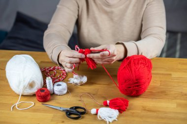 Woman making handmade traditional martisor, from red and white strings with tassel. Symbol of holiday 1 March, Martenitsa, Baba Marta, beginning of spring in Romania, Bulgaria, Moldova