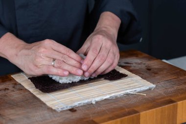 Suşi şefinin ellerini kapatın ve Japon yemeği hazırlayın. Adam restoranda suşi yapmak için pilav pişiriyor. Geleneksel Asya deniz ürünleri kesim tahtasının üzerinde.