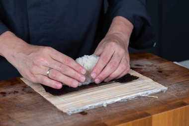 Suşi şefinin ellerini kapatın ve Japon yemeği hazırlayın. Adam restoranda suşi yapmak için pilav pişiriyor. Geleneksel Asya deniz ürünleri kesim tahtasının üzerinde.