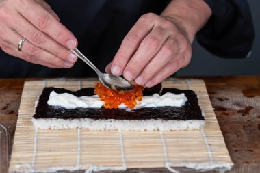 Suşi şefinin ellerini kapatın ve Japon yemeği hazırlayın. Adam restoranda kırmızı havyarla suşi, avokado ve peynir pişiriyor. Geleneksel Asya deniz ürünleri kesim tahtasının üzerinde.