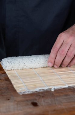 Suşi şefinin ellerini kapatın ve Japon yemeği hazırlayın. Adam restoranda kırmızı havyarla suşi, avokado ve peynir pişiriyor. Geleneksel Asya deniz ürünleri kesim tahtasının üzerinde.