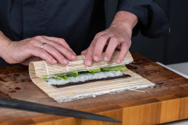 Suşi şefinin ellerini kapatın ve Japon yemeği hazırlayın. Adam restoranda suşi pişiriyor. Geleneksel Asya deniz ürünleri kesim tahtasının üzerinde.