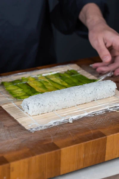 寿司職人の手を閉じて日本料理を準備する レストランでは 赤いキャビアとアボカドとチーズで寿司を調理する男 伝統的なアジアの魚介類はまな板に転がる — ストック写真