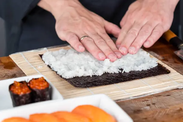 Suşi şefinin ellerini kapatın ve Japon yemeği hazırlayın. Adam restoranda kırmızı havyarlı ve somonlu suşi pişiriyor. Geleneksel Asya deniz ürünleri kesim tahtasının üzerinde.