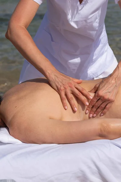 在海滩上的热带按摩浴中放松的女人在海边的按摩床上 专业按摩师提供背部及颈部水疗服务 — 图库照片