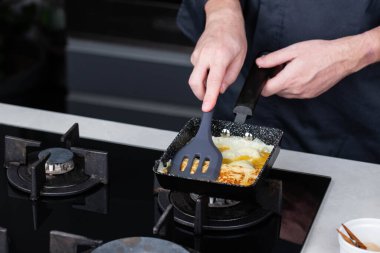 Aşçı elleri Tamagoyaki ya da Tamago geleneksel Japon usulü rulo omlet tarifi pişirirken çırpılmış çırpılmış yumurtaları tavaya sararak dikdörtgen şeklinde omlet yapıyor..