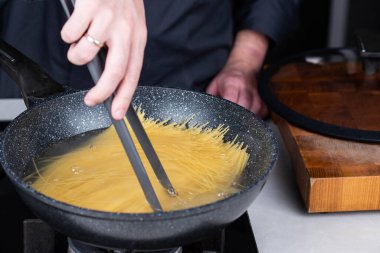 Profesyonel aşçılar İtalyan Capellini spagetti makarnası yapıyorlar modern mutfak ocağında kaynar suda tava tenceresinde. Sıcak yemek buharı..