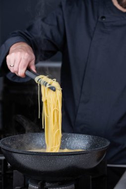 Profesyonel aşçılar İtalyan Capellini spagetti makarnası yapıyorlar modern mutfak ocağında kaynar suda tava tenceresinde. Sıcak yemek buharı..