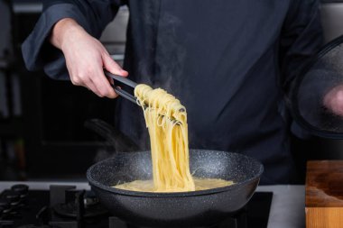 Profesyonel aşçılar İtalyan Capellini spagetti makarnası yapıyorlar modern mutfak ocağında kaynar suda tava tenceresinde. Sıcak yemek buharı..