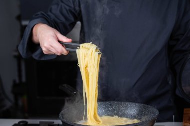 Profesyonel aşçılar İtalyan Capellini spagetti makarnası yapıyorlar modern mutfak ocağında kaynar suda tava tenceresinde. Sıcak yemek buharı..