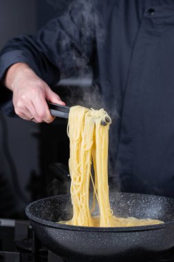 Profesyonel aşçılar İtalyan Capellini spagetti makarnası yapıyorlar modern mutfak ocağında kaynar suda tava tenceresinde. Sıcak yemek buharı..