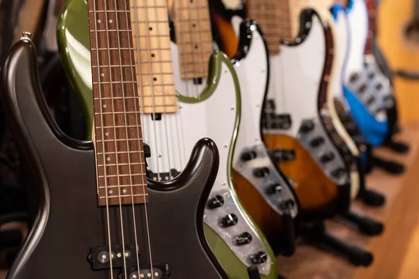 Closeup of row of different colorful bass guitars on the display for sale hanging in a music shop