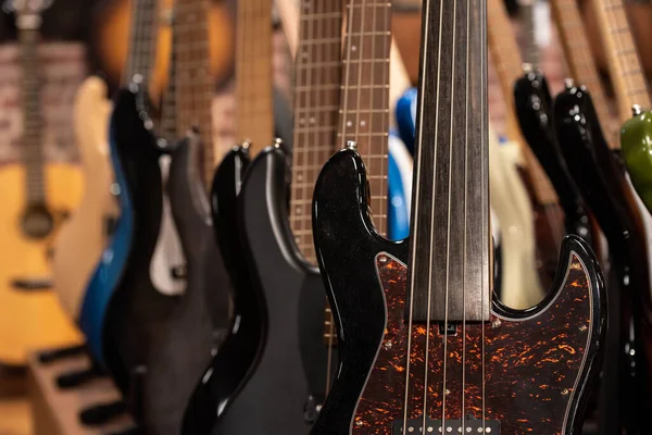 Closeup of row of different colorful bass guitars on the display for sale hanging in a music shop