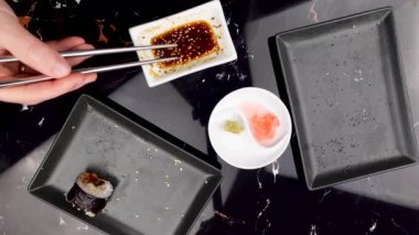 Japon yemeklerini yiyen çubuklarla ellerini yaklaştır. Geleneksel Asya dürümleri. Sebzeli ve ton balıklı Maki suşisi. Wasabi ve Soya sosu kasede.