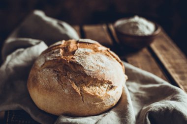 Masada bez peçeteyle ekmek ve buğday unu tozu. Ahşap masa üstünde ev yapımı ekmek pişirme konsepti