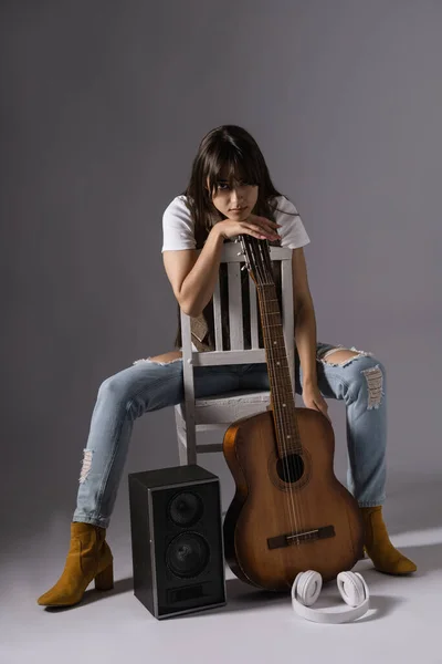 若い女性が椅子に座っているクラシックギターを保持しています アコースティックギターとミュージックコラム近くのスタジオでミュージシャン ストック写真