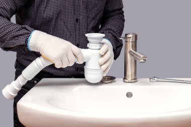 Bir muslukçu banyoya lavabo için sifon yerleştirir.